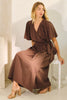 Woman wearing a brown dress sitting on a white stool against a neutral background