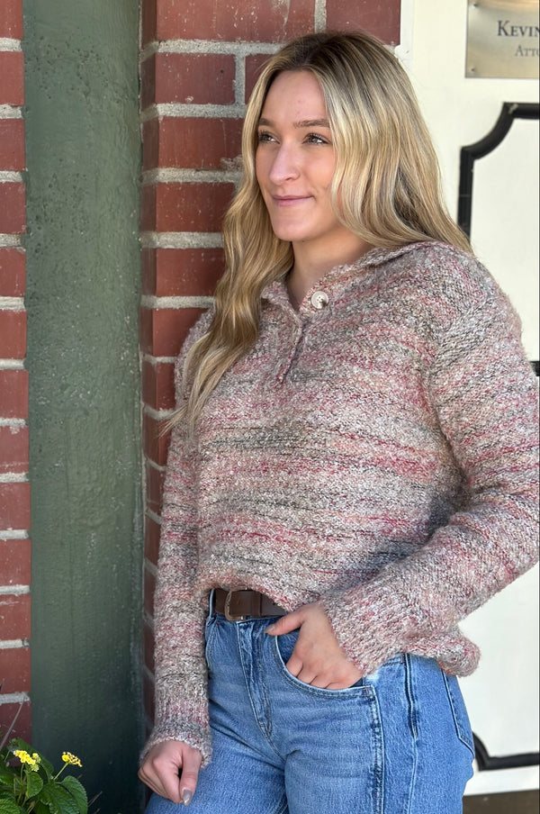 Woman wearing a patterned sweater and jeans standing against a brick wall.