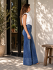 Woman wearing blue jeans and a white top standing outdoors near a building.