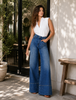 Woman wearing a white sleeveless top and high waisted blue wide-leg jeans standing outdoors.