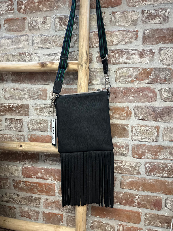 Black fringe bag hanging on a broom against a brick wall