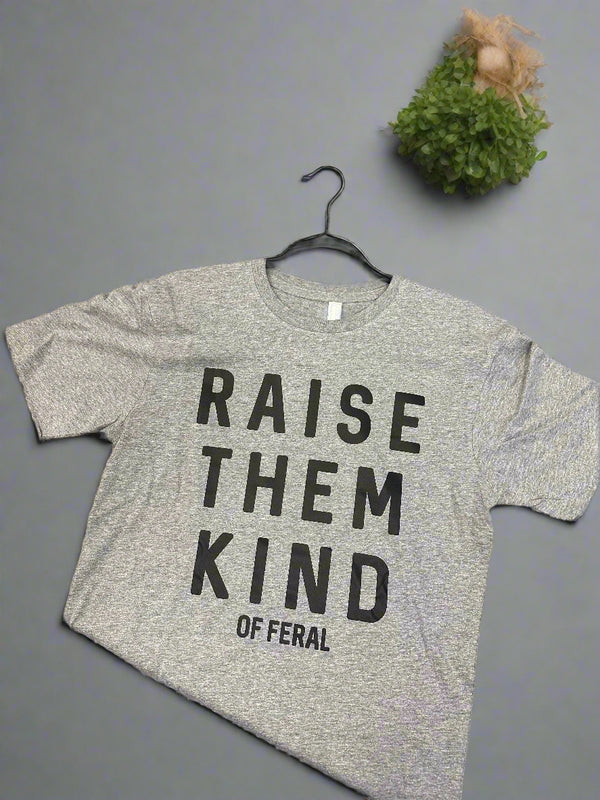 Gray Tshirt with 'Raise Them Kind' text on a wooden surface