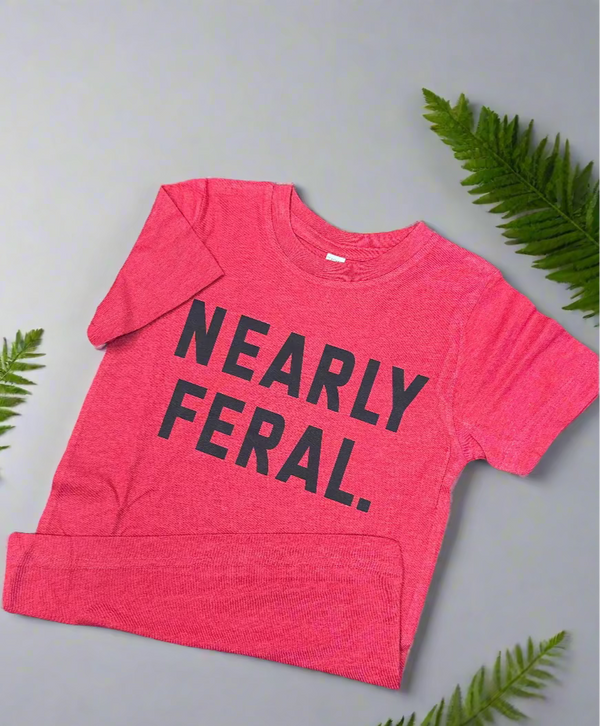 Red t-shirt with 'NEARLY FERAL' text on a wooden surface