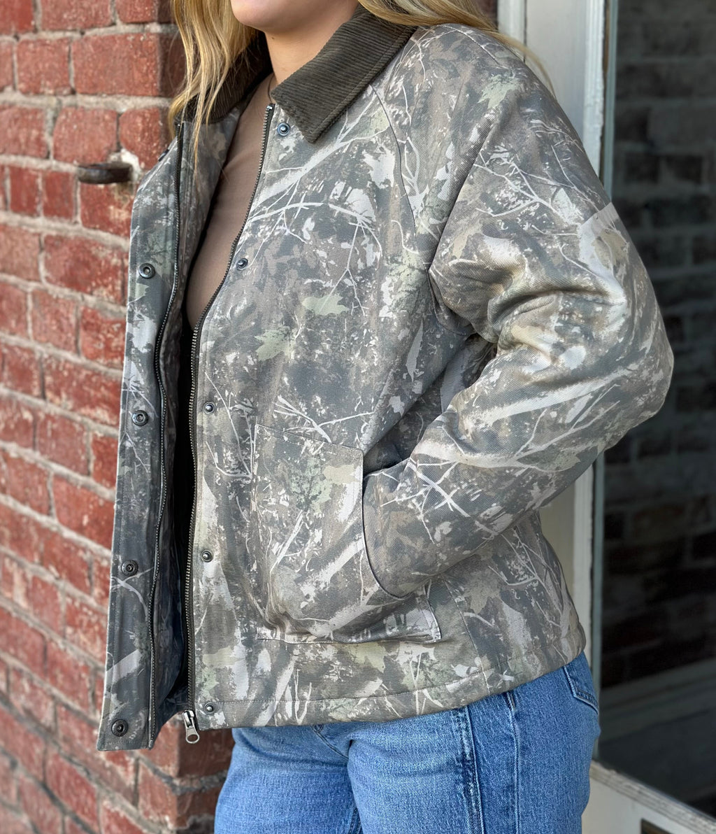 Person wearing a camouflage jacket standing against a brick wall.