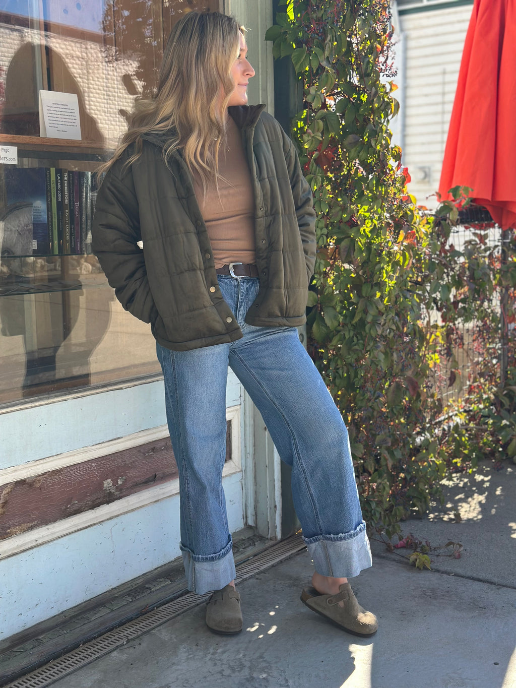 Woman standing outside a store with a green jacket and blue jeans.