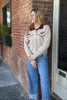 Woman wearing a patterned cardigan and jeans standing against a brick wall.
