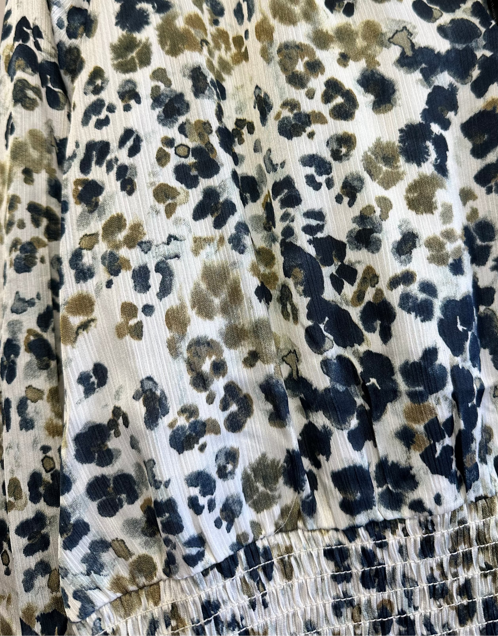 A close-up of a patterned fabric garment featuring a black, navy, and olive-brown abstract spotted print on a cream background, with a smocked elastic waist.