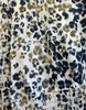 A close-up of a patterned fabric garment featuring a black, navy, and olive-brown abstract spotted print on a cream background, with a smocked elastic waist.