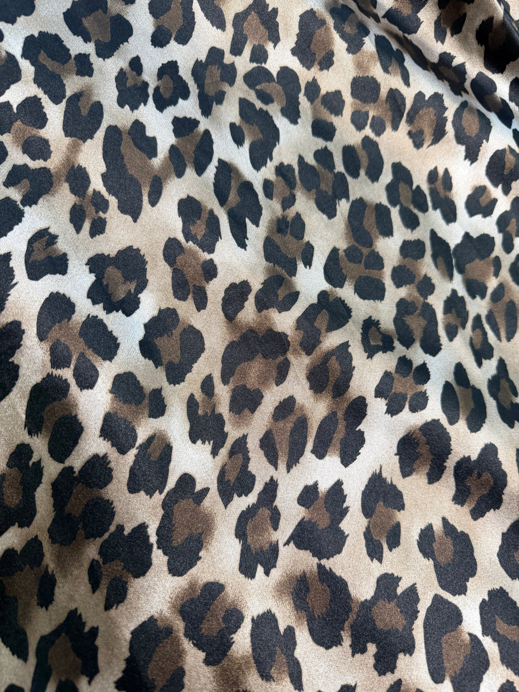 Close-up of leopard print fabric with a greige base and irregular black and brown spots.