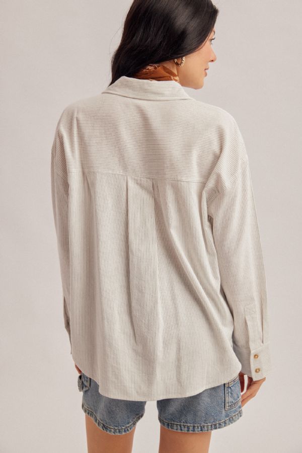 A woman shown from the back wearing a light beige textured button-up shirt and denim shorts against a plain light gray studio background.