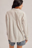 A woman shown from the back wearing a light beige textured button-up shirt and denim shorts against a plain light gray studio background.