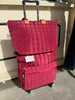 A red quilted rolling suitcase with a matching top tote bag, both featuring light brown leather accents and white price tags, set against a beige wall and concrete floor.