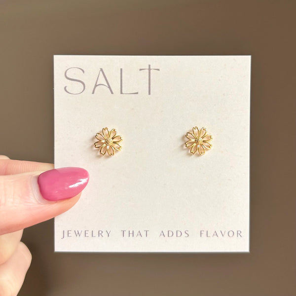 Gold flower earrings on a 'SALT' branded card held by a hand with pink nail polish.
