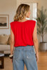 Woman wearing a red sleeveless bubble hem top and blue jeans in a living room setting