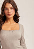 Woman wearing a gray ribbed long-sleeve top and pink skirt on a plain background